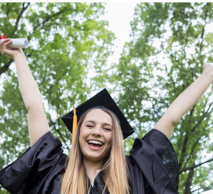 A graduate celebrating outdoors in cap and gown